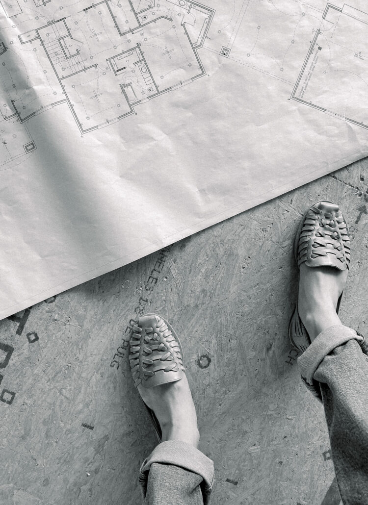 Blueprints rolled out on ground with woman's shoes standing next to them.