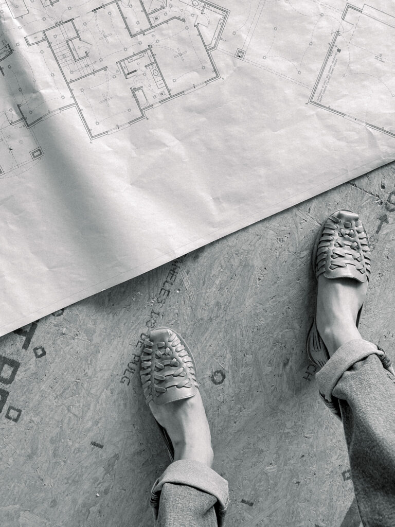 Blueprints rolled out on ground with woman's shoes standing next to them.